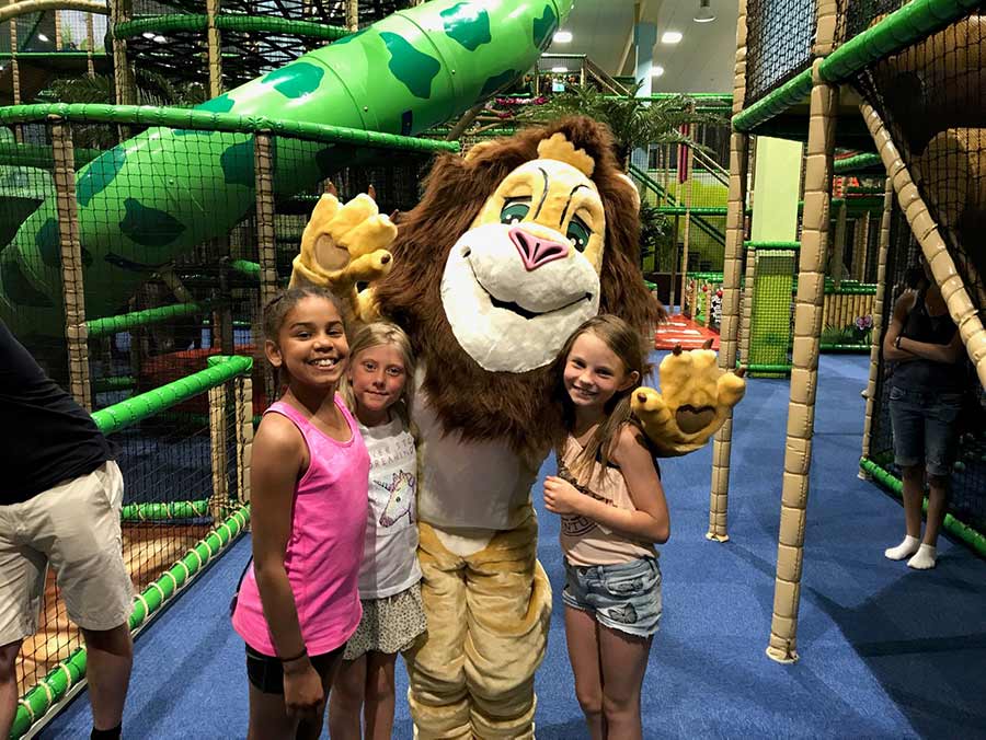 Person utkledd som løve poserer med tre smilende jenter på rundt 10 år. Leo's Lekeland kan sees i bakgrunnen. Barnebursdag i Oslo